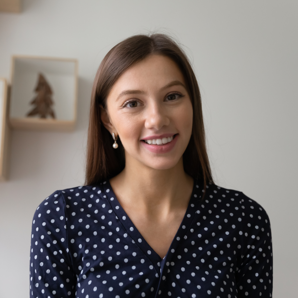 Smiling young woman in a polka dot blouse, posing against a minimalist background.